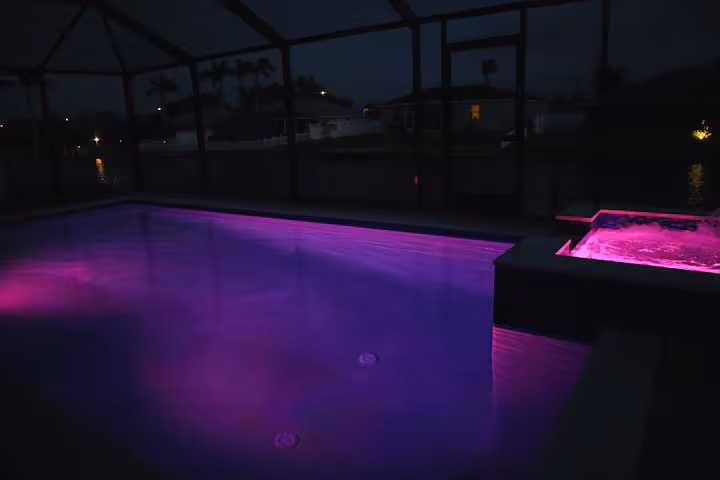 Private pool and spa glowing with purple LED lighting after dark